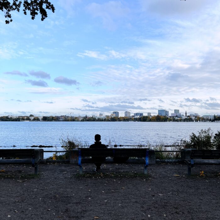 Blick über die Alster auf St. Georg, im Vordergrund ein Mann auf einer Bank, man sieht ihn von hinten