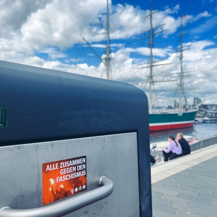 Ein Aufkleber an einem Mülleimer an der Hafenpromenade: "Alle zusammen gegen den Faschismus". Im Hintergrund das Museumsschiff Rickmer Rickmers.