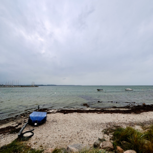 Ein kleines, blaues Boot liegt kieloben am Strand von Wackerballig, dahinter aufgewühlte See, ein Sturmtag