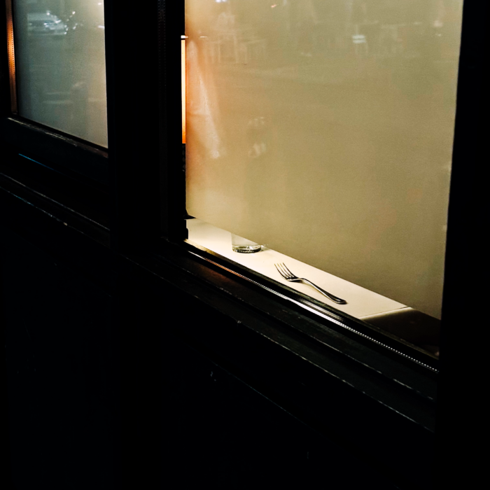 Blick von außen in ein Restaurantfenster, man sieht nur eine Gabel auf einem Tisch