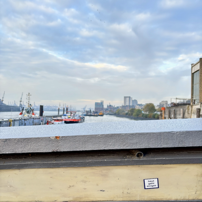 Die Elbe im Hafen bei Sonnenaufgang, im Vordergrund ein Aufkleber an einem Geländer: "Heute geht einiges"