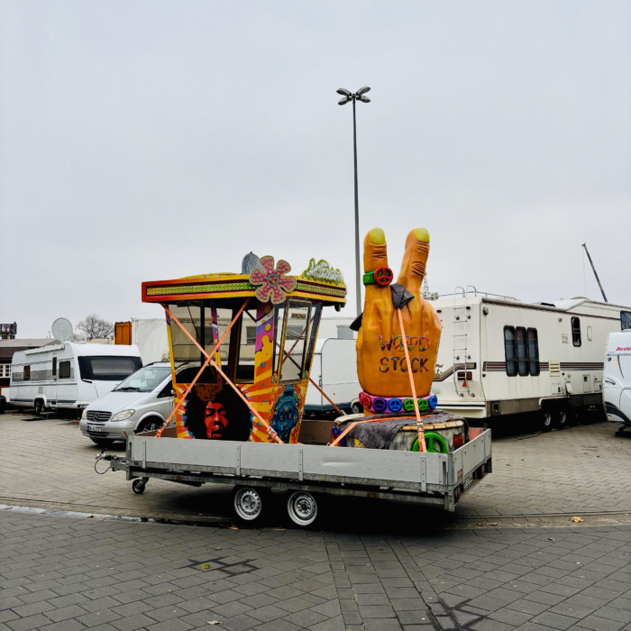 Dekoelemente von Fahrgeschäften auf dem Dom, noch auf einem Anhänger, ein Kassenhäuschen, eine große Plastikhand mit dem Peace-Zeichen und "Woodstock"-Aufschrift auf dem Handrücken