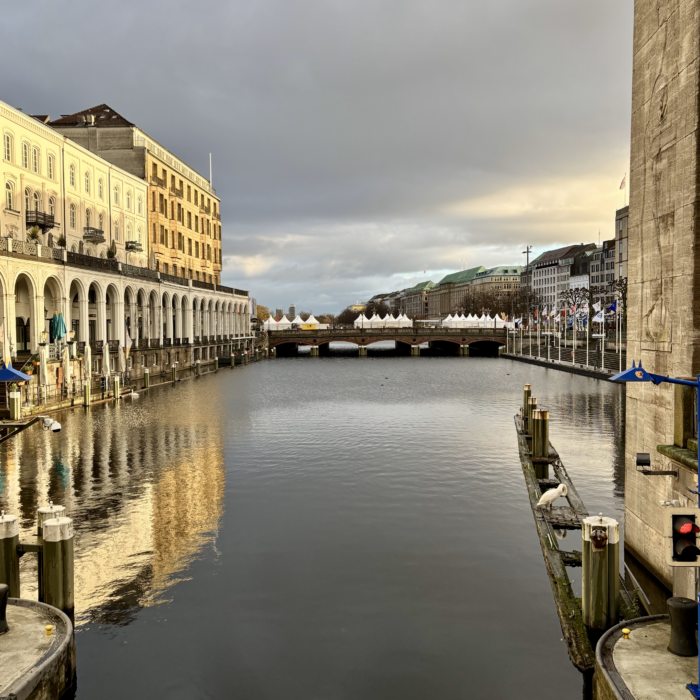 Die Rathausarkaden im Morgenlicht, auf der Brücke im Hintergrund die Weihnachtspavillons am Jungfernstieg