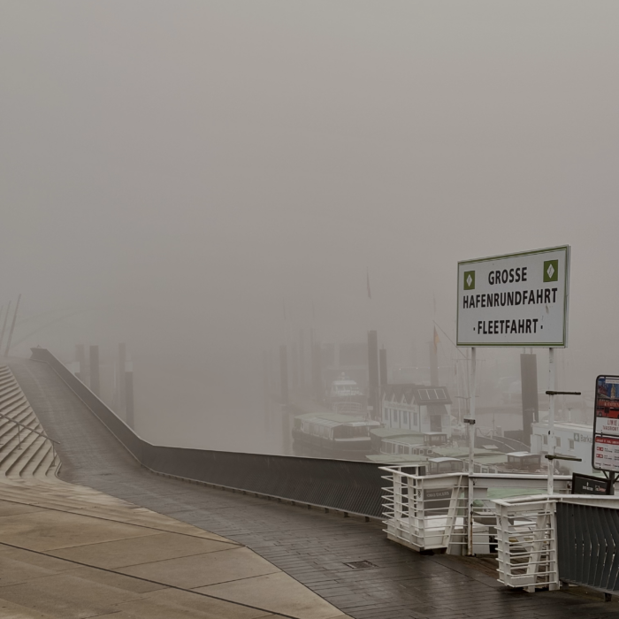 Die Hamburger Hafenpromenade im dichten Nebel, an der Kaimauer ein Schild "Grosse Hafenrundfahrt"