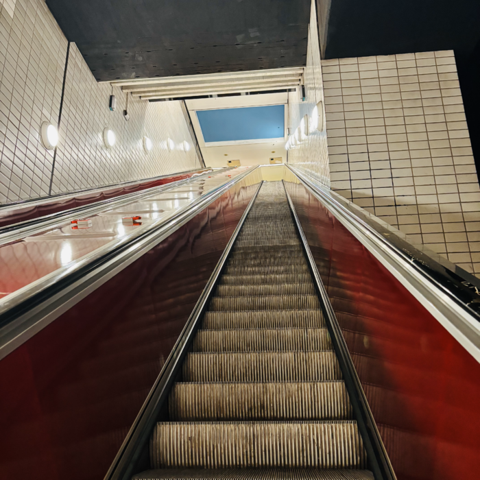 Rolltreppen im U-Bahnbereich des Hauptbahnhofs, von unten fotografiert, oben ein Stück blau angemalter Decke