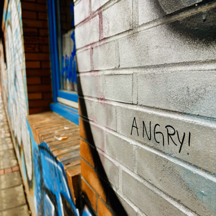 Ein Edding-Schriftzug "Angry" an einer mit Graffiti verzierten Außenmauer eines Kindergartens